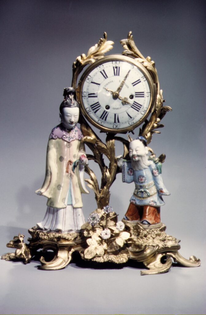 Mantel clock of about 1745-49 with a gilt-bronze scrolling frame holding a white dial above two porcelain Chinese figures on a flowering gilt-bronze base