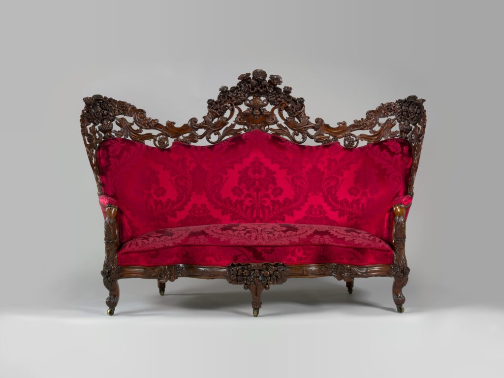 Rosewood sofa with a pierced, carved crest of flowers and scrolls along the back, red damask upholstery and curved legs, on a gray ground