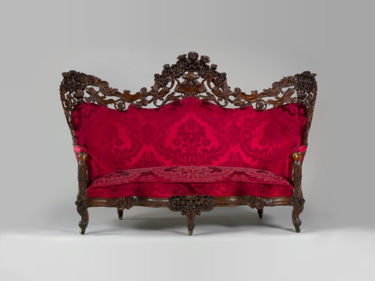 Rosewood sofa with a pierced, carved crest of flowers and scrolls along the back, red damask upholstery and curved legs, on a gray ground