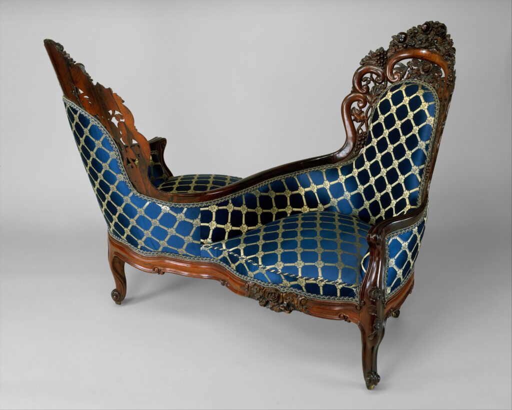 Rosewood seat with two sides facing opposite ways, joined in the middle, upholstered in blue fabric woven with a gold lattice pattern, with a carved floral crest and curved legs