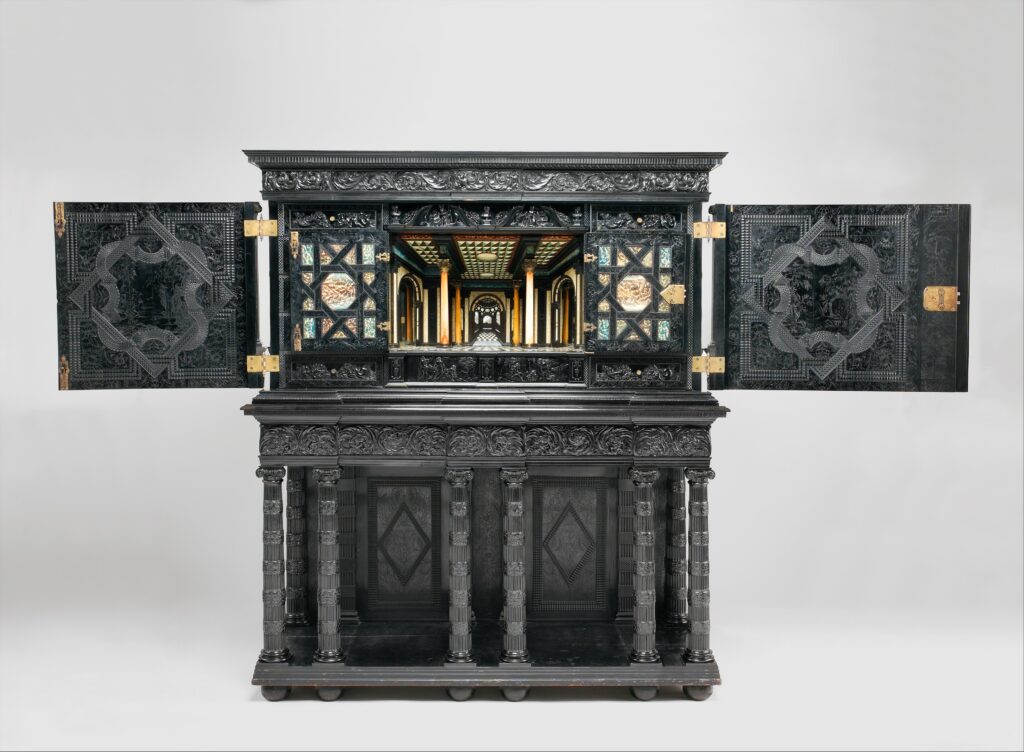 Black ebony cabinet on a stand with carved columns, its doors open to show a brightly colored architectural interior with a mirrored recess