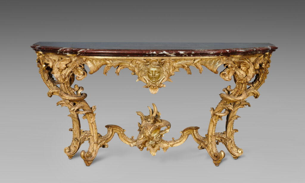 Gilded carved console table with a shaped dark red marble top, a gilt mask at the centre of the frieze, S-shaped legs topped with carved dragons and a stretcher with a helmet at the centre