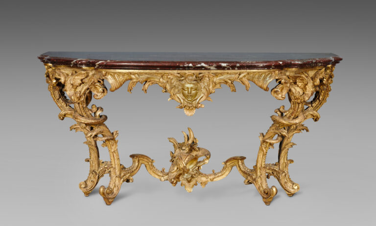 Gilded carved console table with a shaped dark red marble top, a gilt mask at the centre of the frieze, S-shaped legs topped with carved dragons and a stretcher with a helmet at the centre
