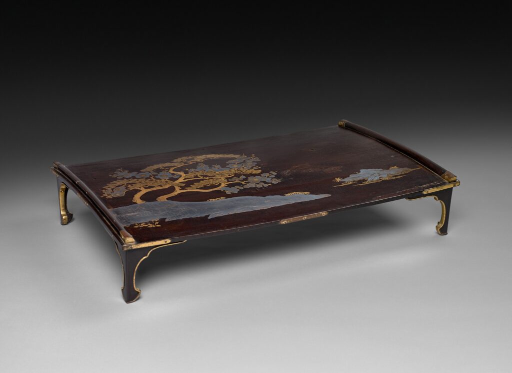 Japanese Furniture Low black lacquer writing table with a gold and silver pine design, a slightly curved top edge and four short curved feet with metal caps