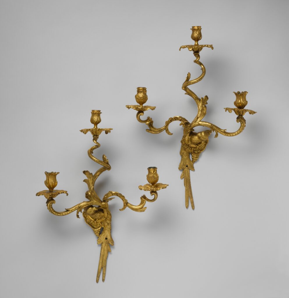 Two gilded wall brackets, each with three curving candle arms ending in tulip-shaped sockets, scrolling leaves and long tail feathers hanging below, on a grey ground