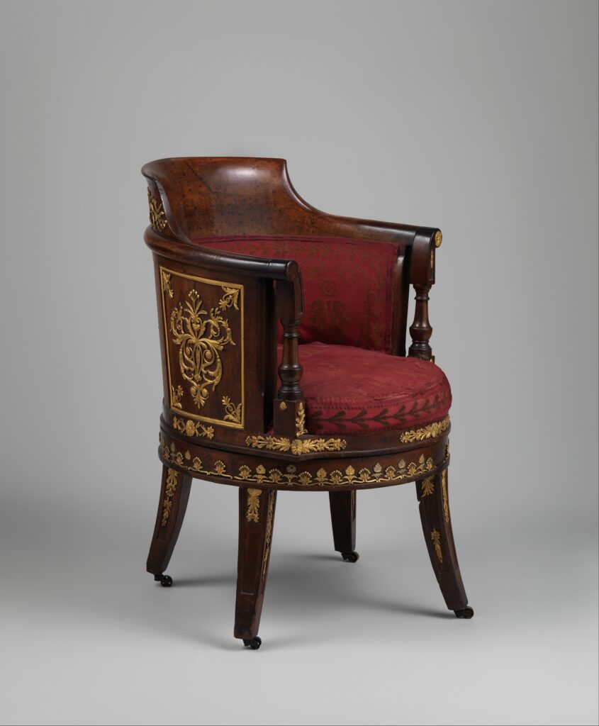 Mahogany desk chair with a rounded barrel back, curved sabre legs, a red upholstered seat and gilt-bronze mounts, on a grey ground