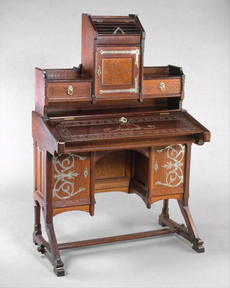 Eastlake Furniture Oak writing desk on a trestle base with angled front legs, a raised cabinet under a pitched lid, incised geometric decoration and metal strap hinges on the lower cupboard doors