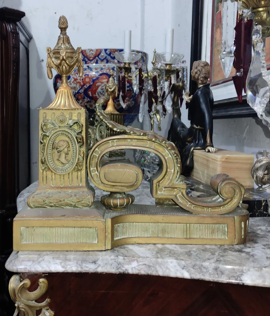 Gilt metal chenet with cameo medallion, urn finial and scroll arm on marble