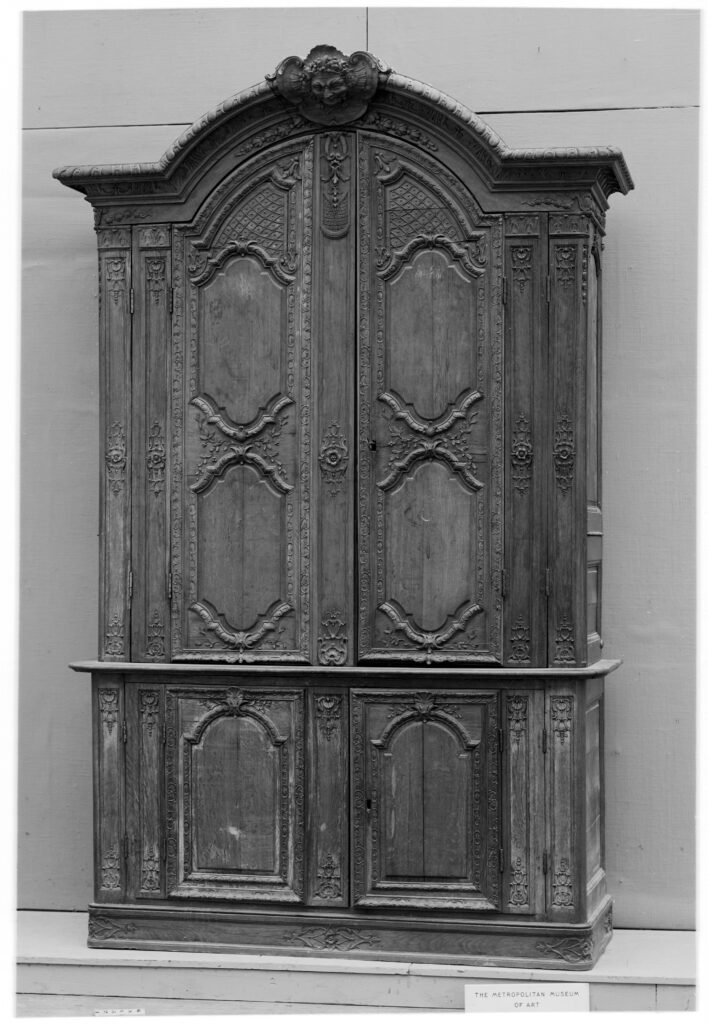 Black-and-white photograph of a two-part antique French armoire in oak, with a domed top, four paneled doors and carved scrolling frames