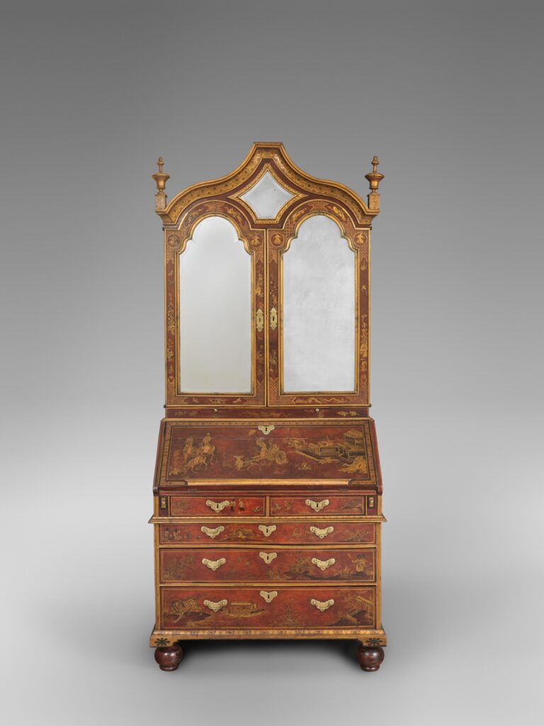 Tall British desk and bookcase of 1700-1720 with two arched mirrored doors above a sloping writing lid and four drawers, the whole surface painted in gold figures on a red ground, standing on turned feet
