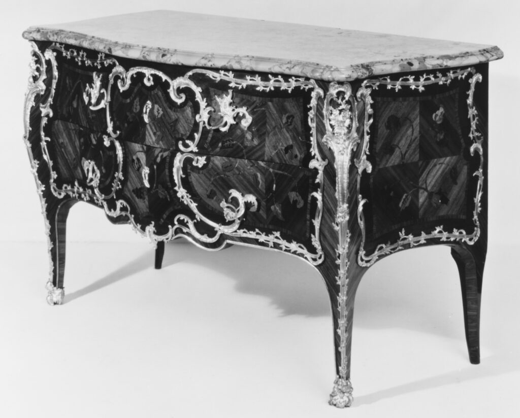 Black-and-white photograph of an antique French commode with a serpentine bombé front, curved legs, scrolling metal mounts and a pale marble top
