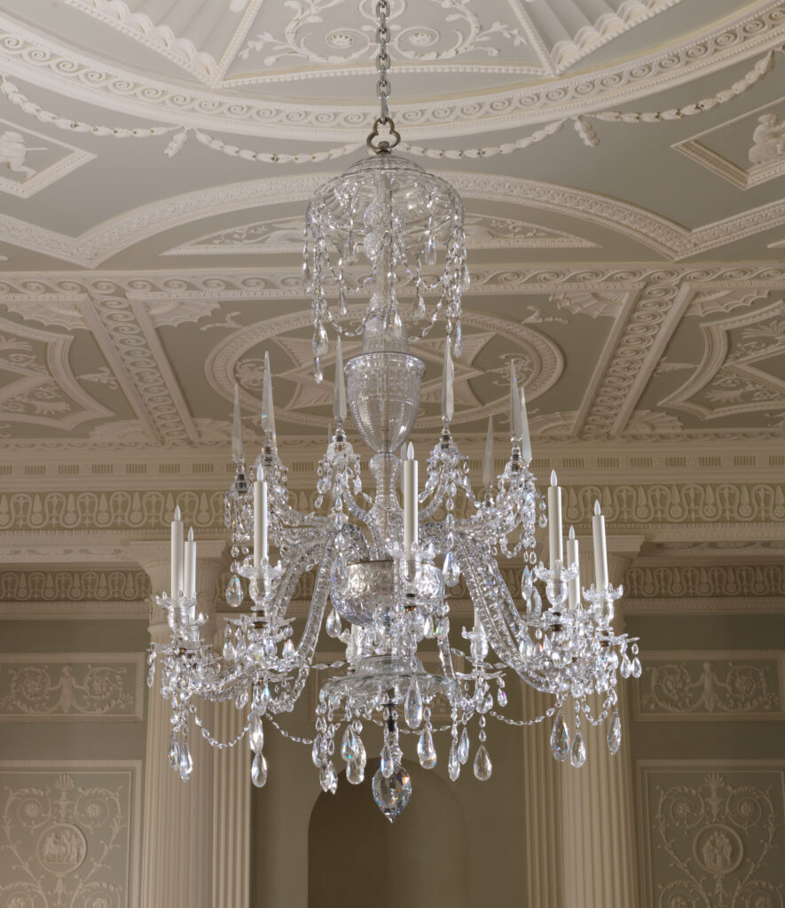 Cut-glass chandelier with tiers of curving arms and long strings of crystal drops, hanging from the centre of a decorated plaster ceiling