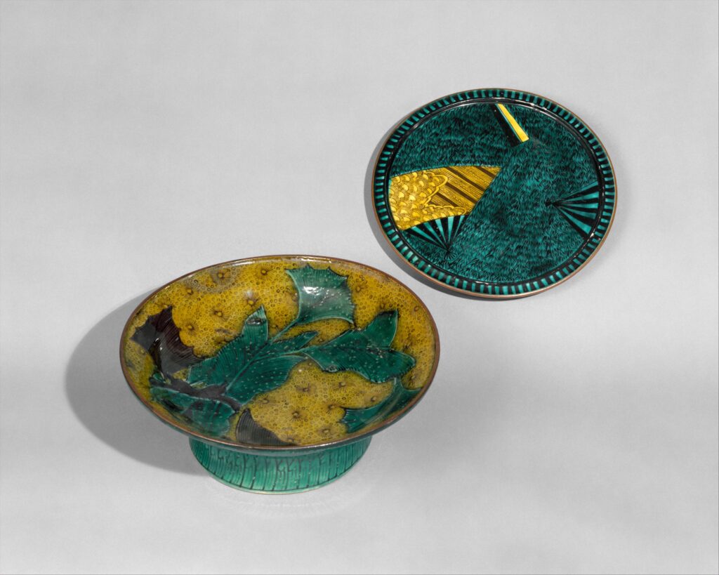 A green footed dish and a green plate with yellow, black and green painted patterns