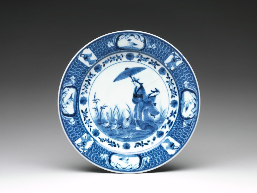 Antique Japanese porcelain plate painted mainly in blue and white, with a figure under a parasol at the center and a border of small panels and a fine pattern