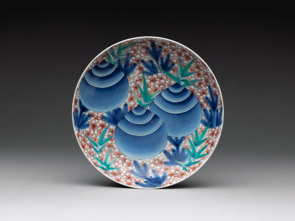 Round dish with large blue rounded forms at the center and a border of red and blue leaf patterns