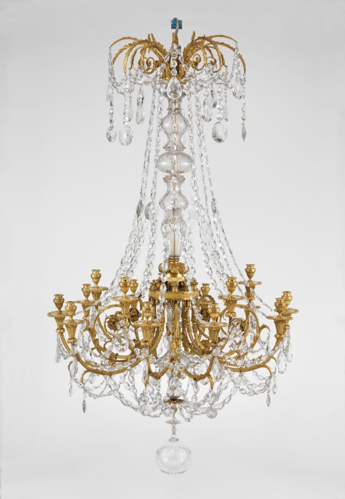 Gilt-bronze chandelier with fifteen candle arms curving out from a glass-covered central shaft, hung with strings of glass drops and a large glass ball at the base