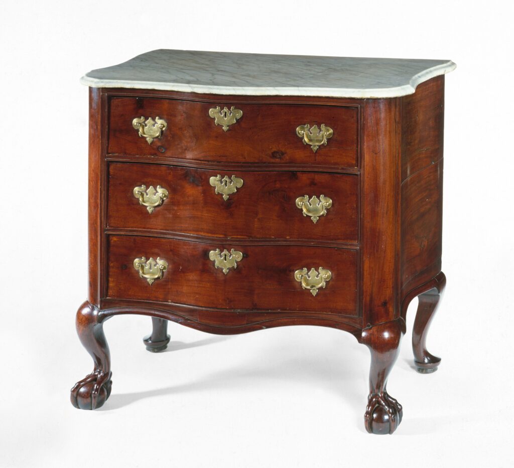 Mahogany chest of drawers by John Goddard, 1755-85, with a serpentine front, three drawers with brass handles, a pale marble-looking top and ball-and-claw feet