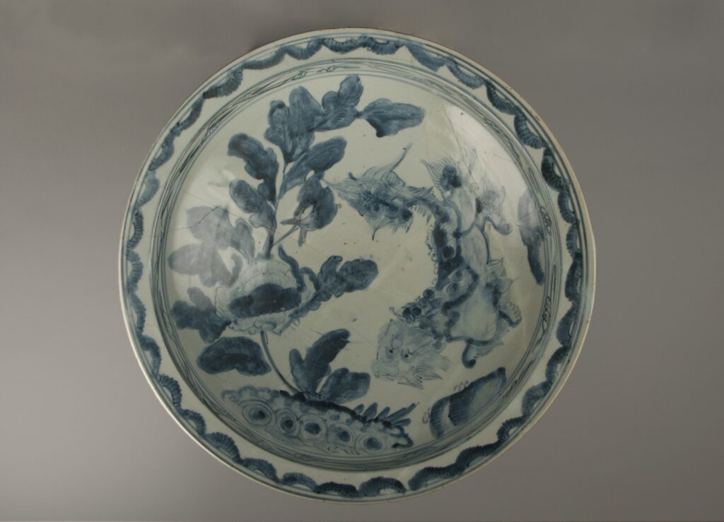 Large round blue-and-white dish with a lion among peony sprays inside a patterned border