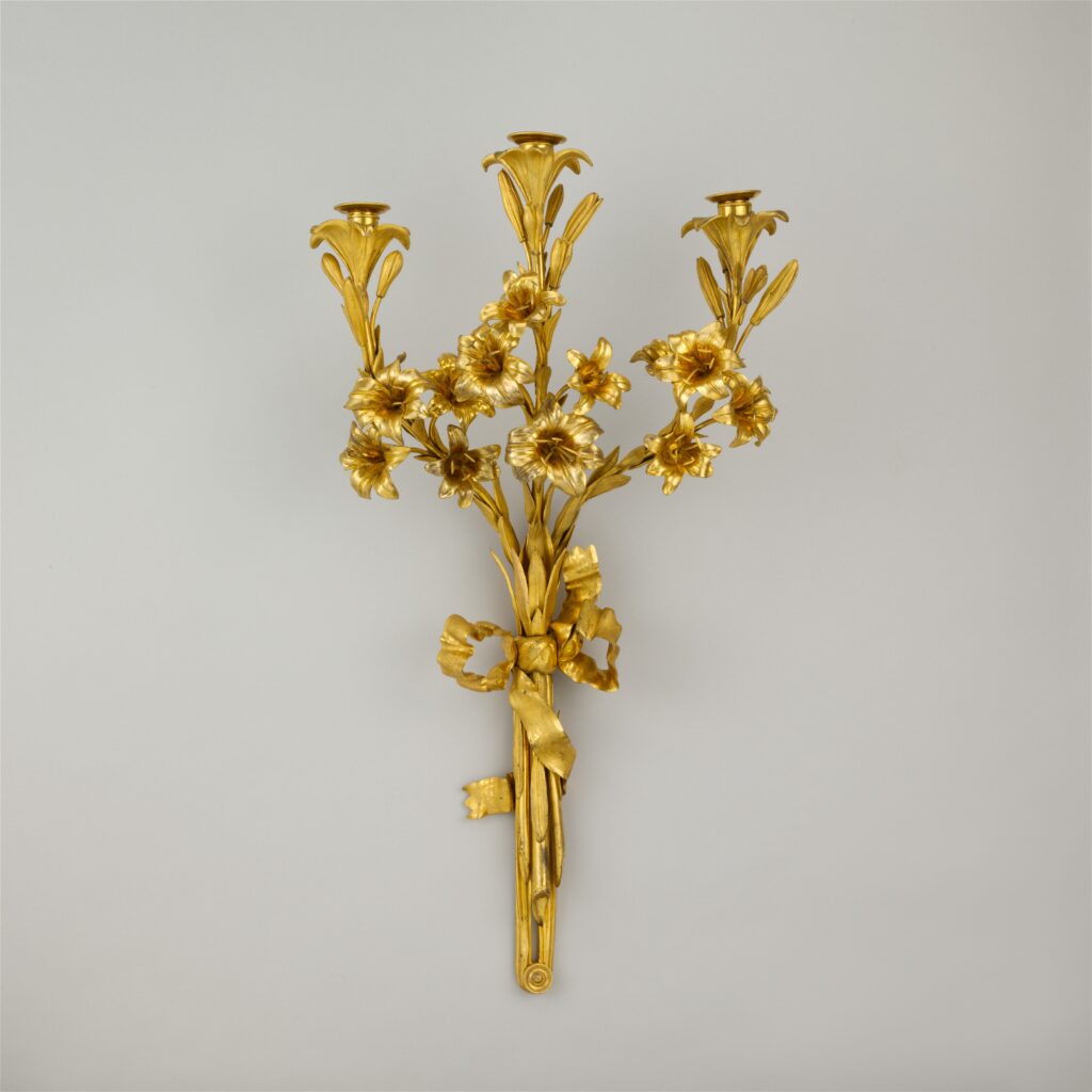 Gilt-bronze wall light shaped like a bunch of lilies tied with a ribbon bow, with three candle cups at the tips of the flower stems