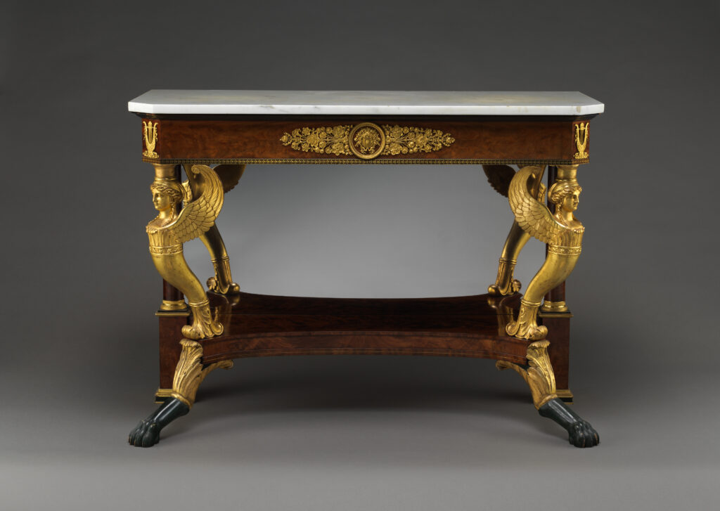 Pier table with a white marble top and gilded winged figures as front supports above dark paw feet, with a lower shelf