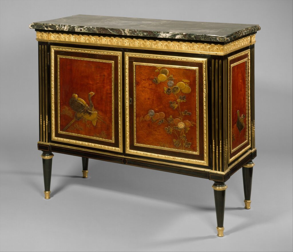 French commode of about 1780-90 with a dark marble top, two doors and sides set with red Japanese lacquer panels painted in gold with birds and flowers, framed in gilt bronze on a black fluted case with four tapering legs