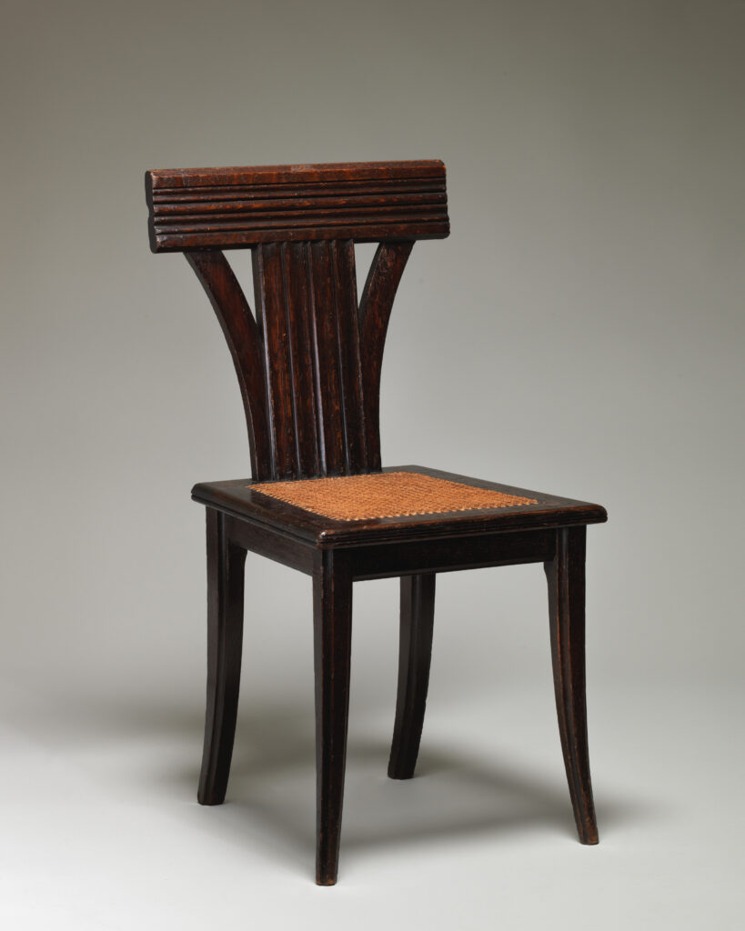 Dark wooden Victorian side chair designed by an architect, with a broad horizontal top rail, a splat of three tapering uprights, flaring legs and a caned seat