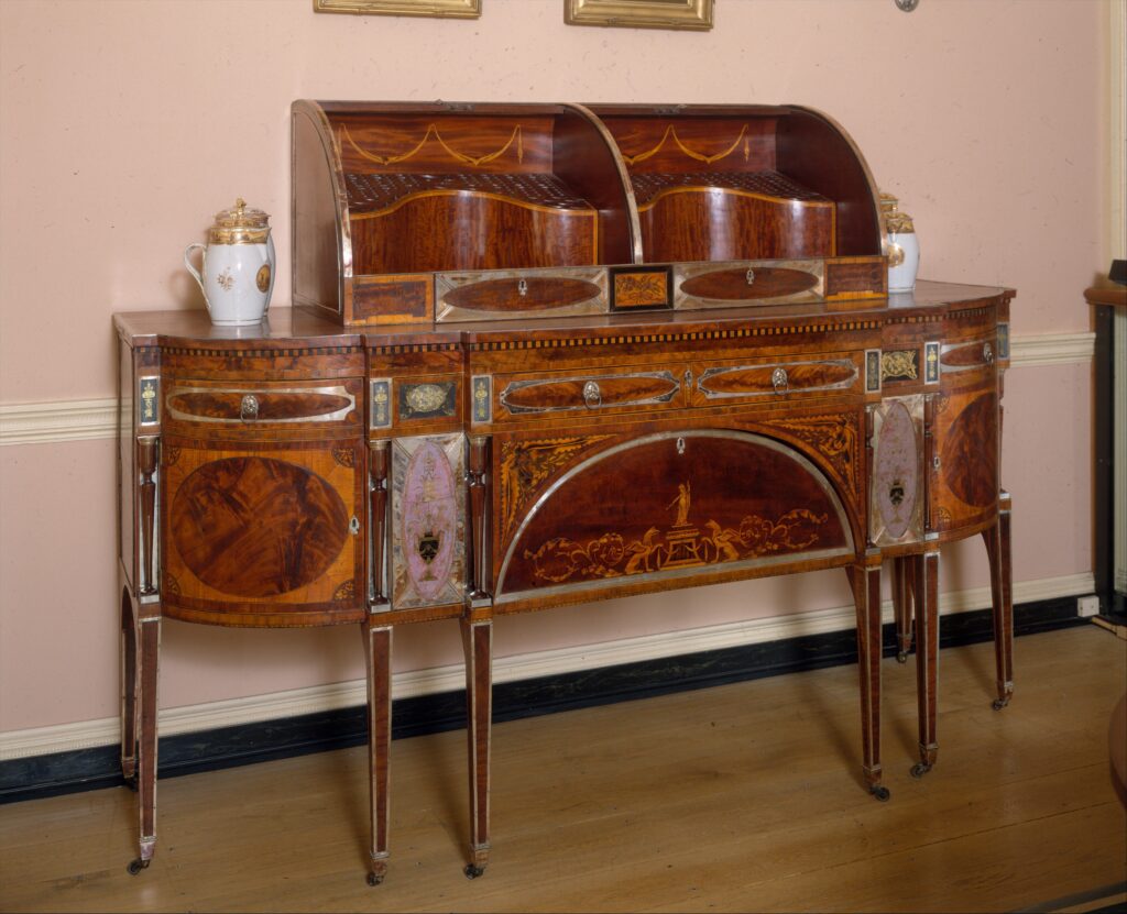 Bow-fronted mahogany sideboard on slender tapered legs with inlaid oval panels and a curved box on top, photographed in a period room