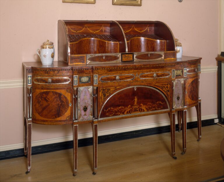Bow-fronted mahogany sideboard on slender tapered legs with inlaid oval panels and a curved box on top, photographed in a period room