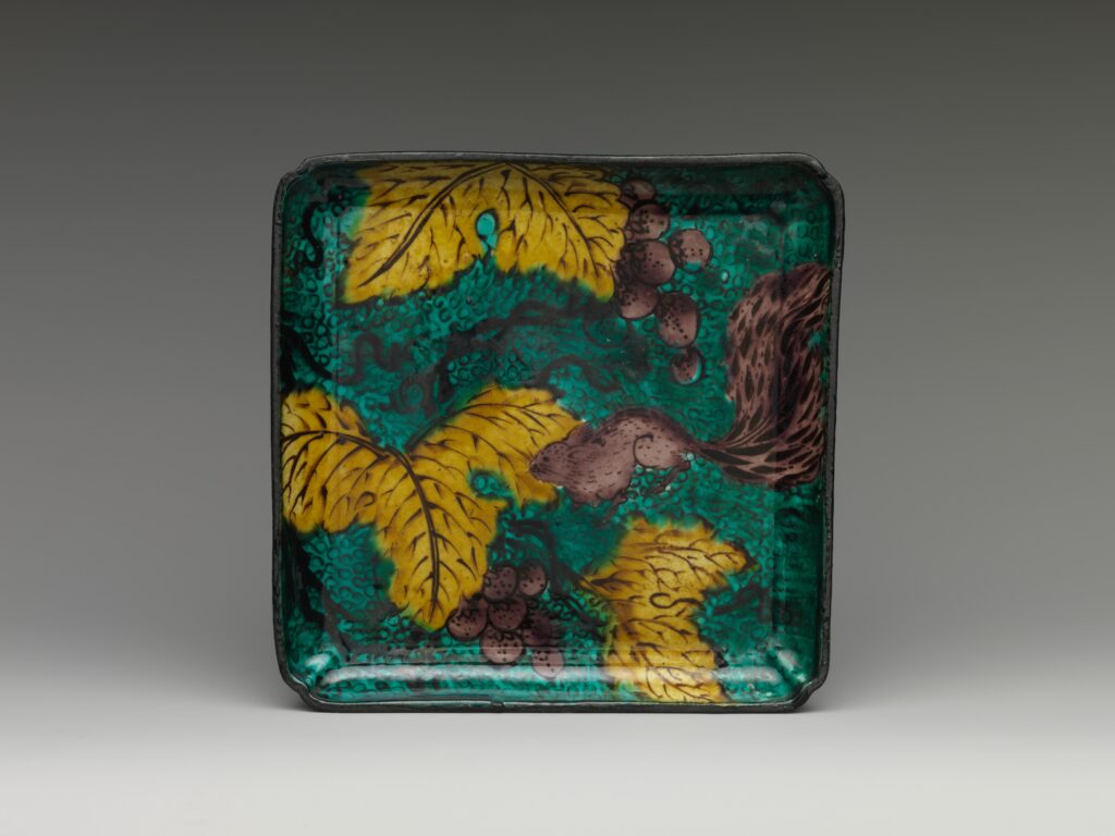 Square green plate with yellow grape leaves, grapes and a brown squirrel