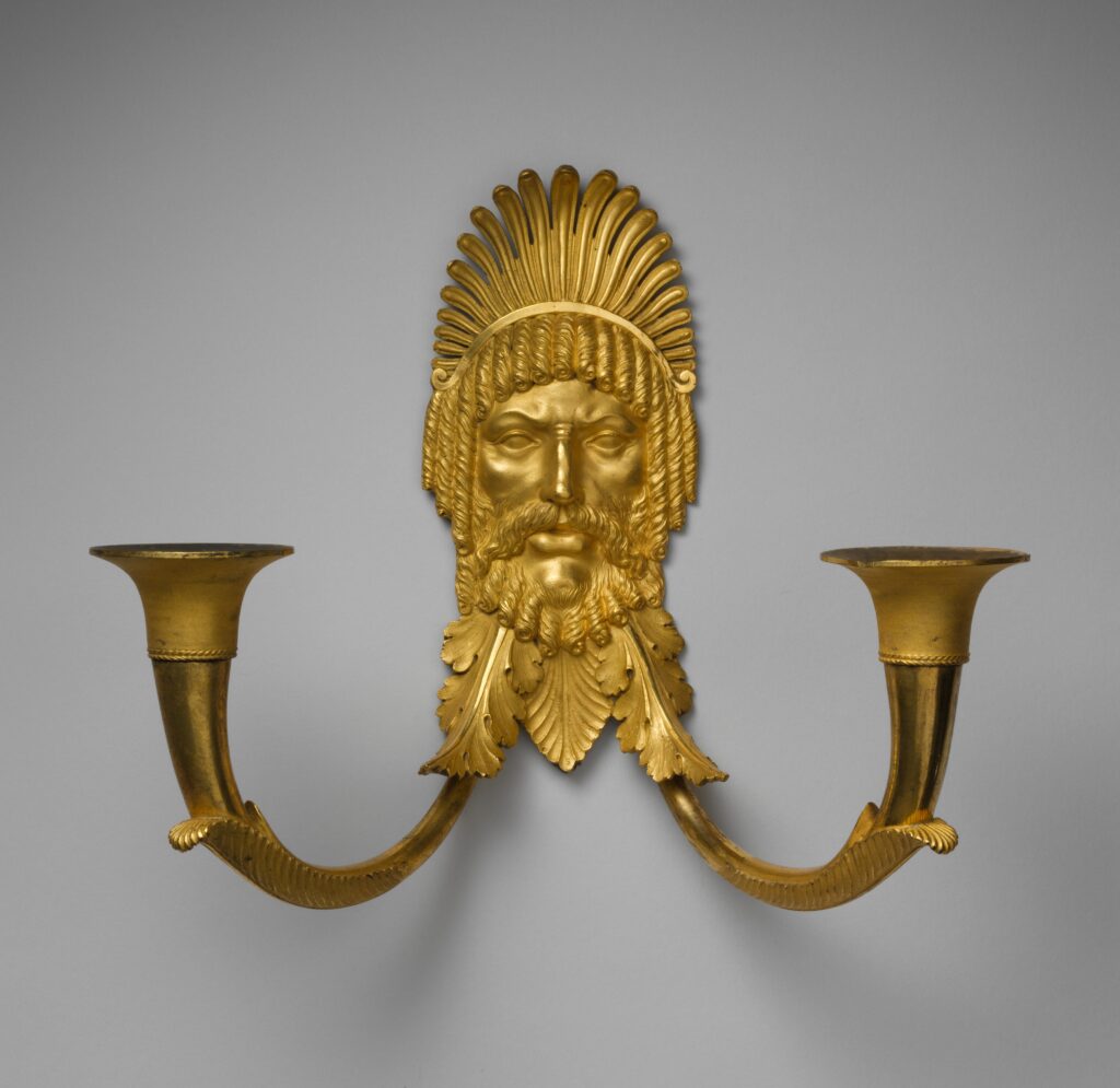 Gilt-bronze wall bracket with a bearded mask under a feathered headdress and two curved horn-shaped arms holding candle cups