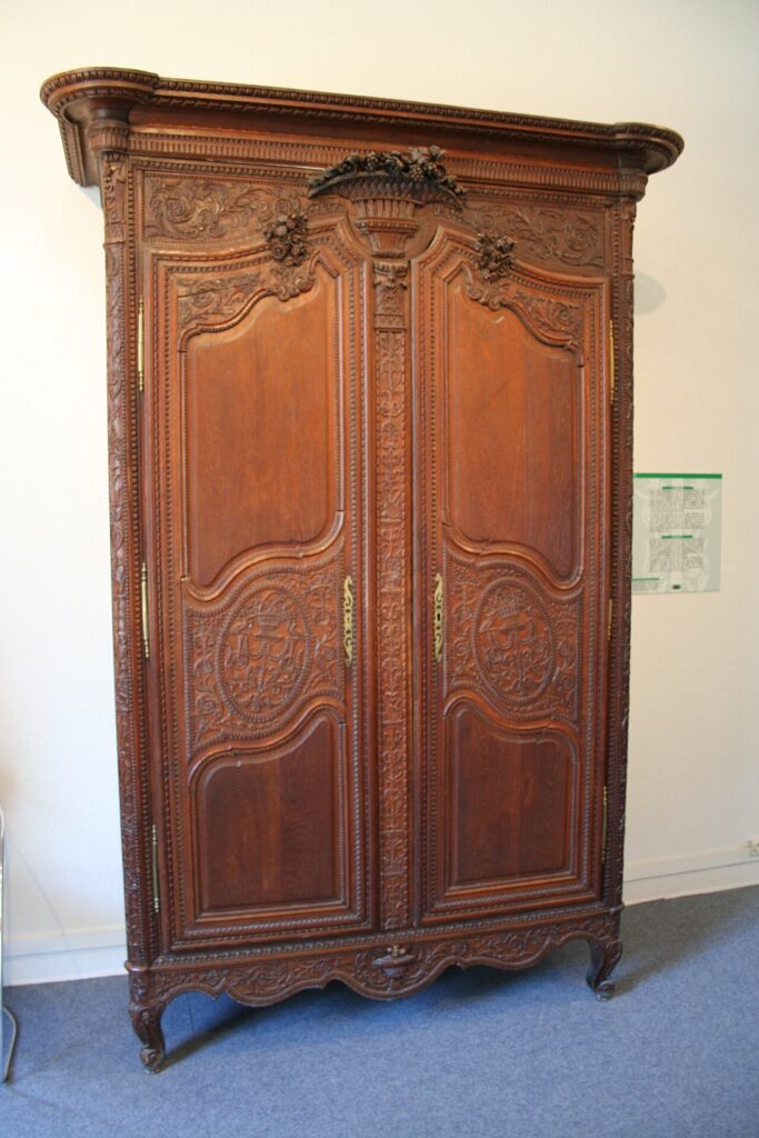 Tall carved wooden armoire from Normandy with a basket of flowers on the cornice, carved oval medallions on both doors, brass hinges and scrolled cabriole feet