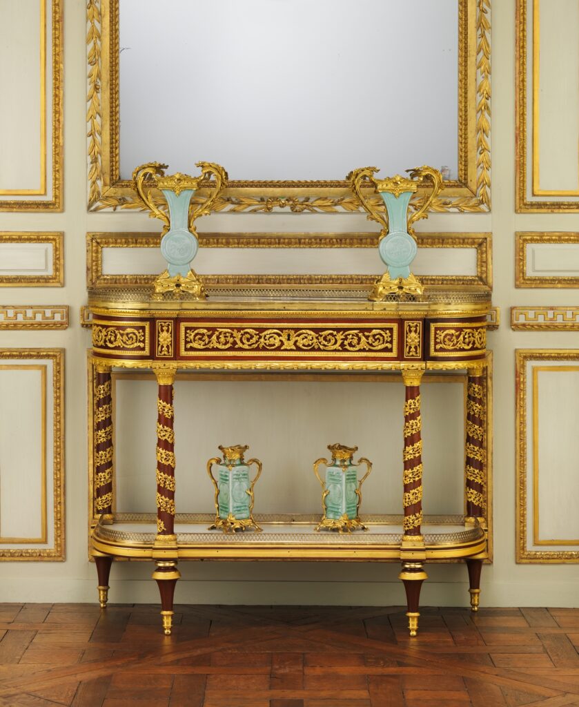Mahogany side table with a drawer frieze, slender legs wound with gilt-bronze ivy, a marble shelf below and a mirror behind, in a period room