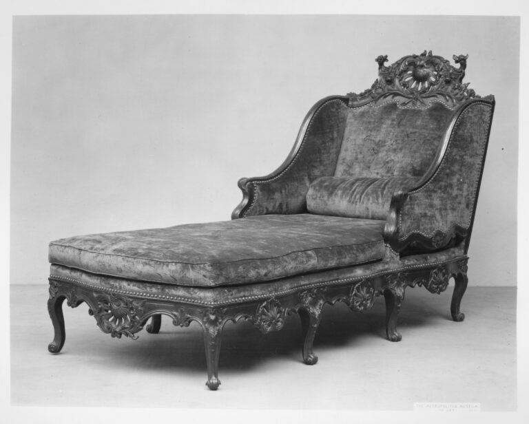 Black-and-white photograph of a long carved walnut daybed with cabriole legs, a carved scalloped apron and a high upholstered back topped by a pierced shell cresting
